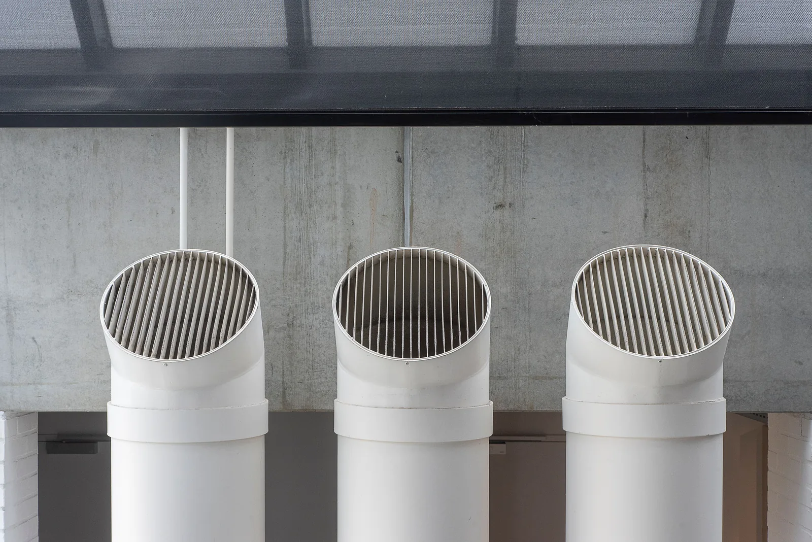 Three circular extract duct outlets fitted to an exposed concrete wall in an industrial building