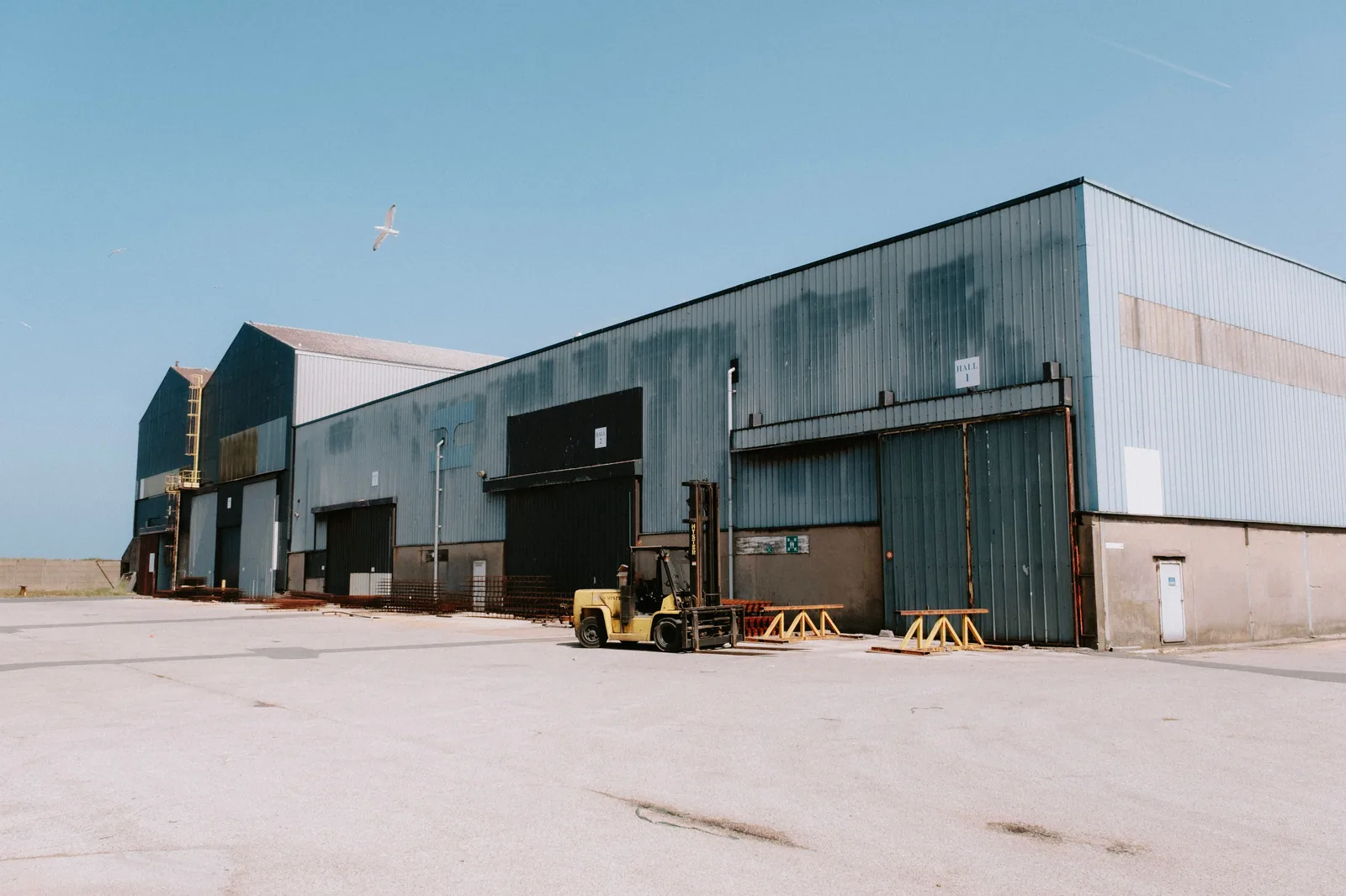 Exterior of an industrial warehouse with loading bay doors and a forklift on the yard
